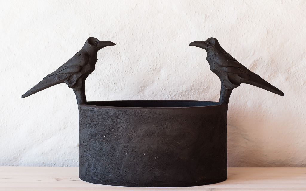 Oval kruka i svart lera med råkor.